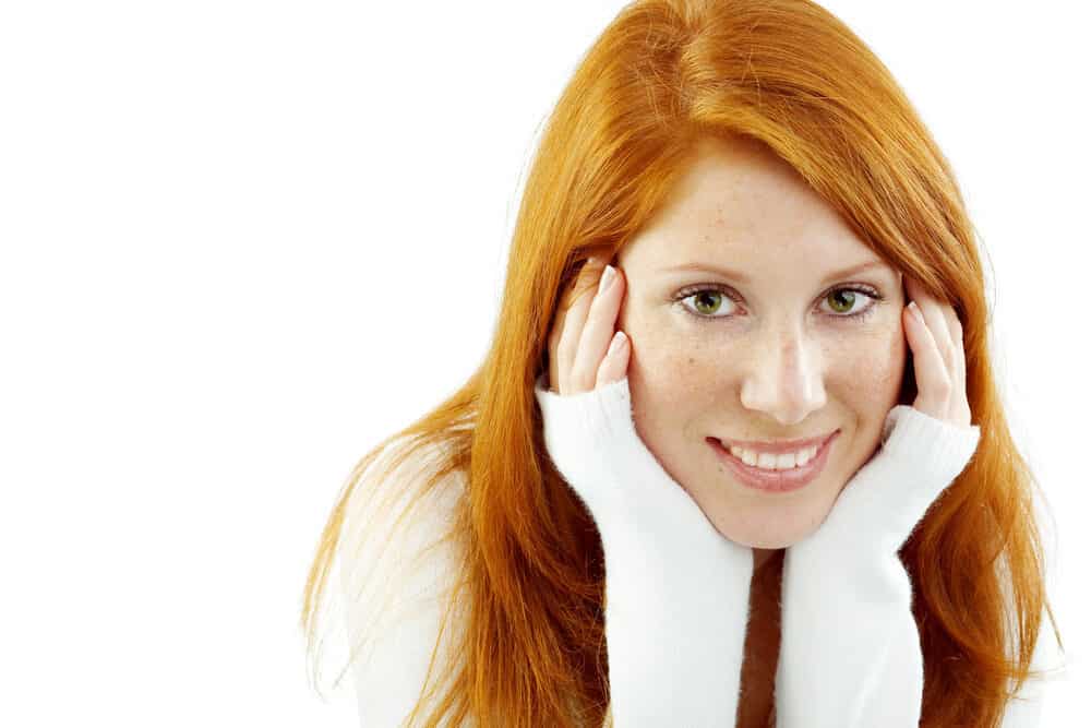 A lady with 1C straight hair wearing bright orange hair after with her hands on her face.