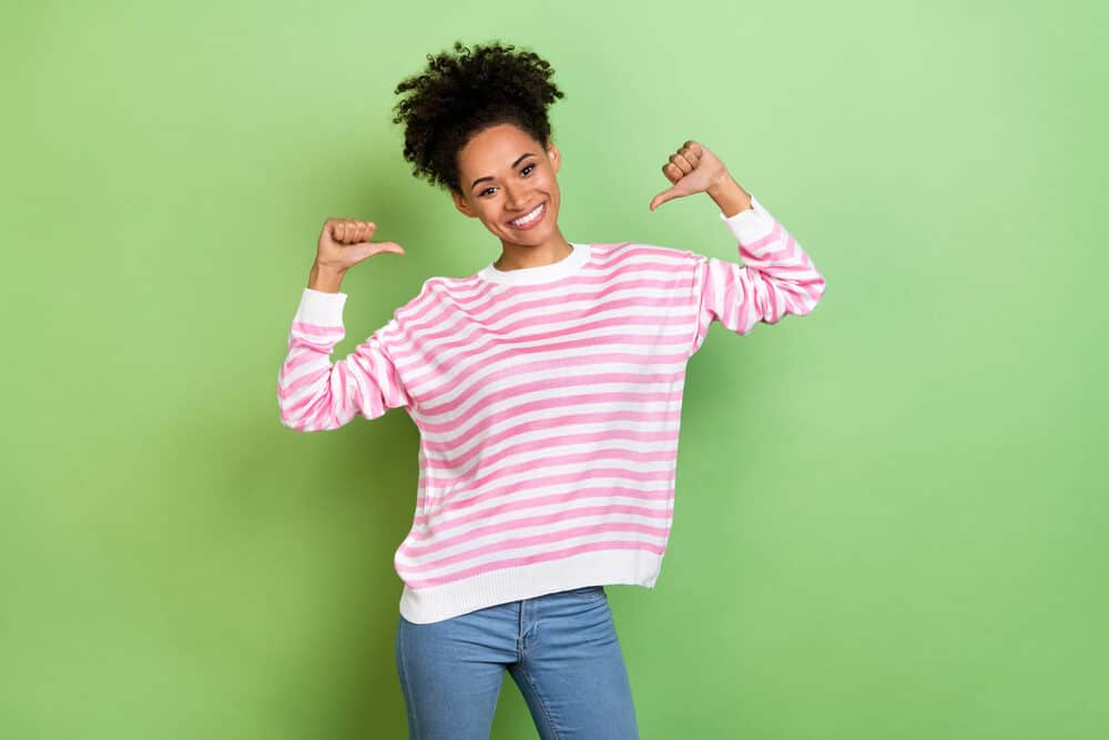 A black lady with natural curls dressed in a pink shirt after using an Olaplex treatment to keep her hair healthy.