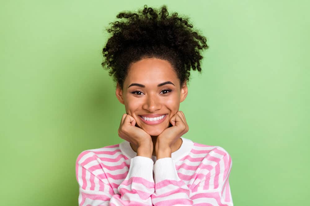 Adorable African American female with unwashed hair in an updo pineapple style wearing pink lipstick.