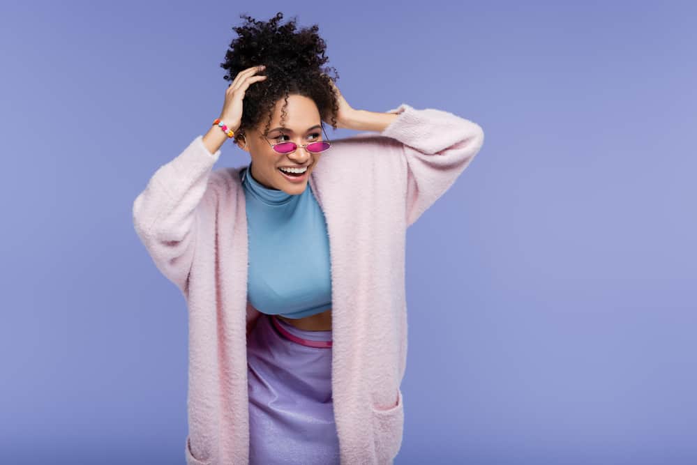 Adult female wearing a pink jacket, blue shirt, and purple skirt is massaging her scalp to maintain healthy hair.