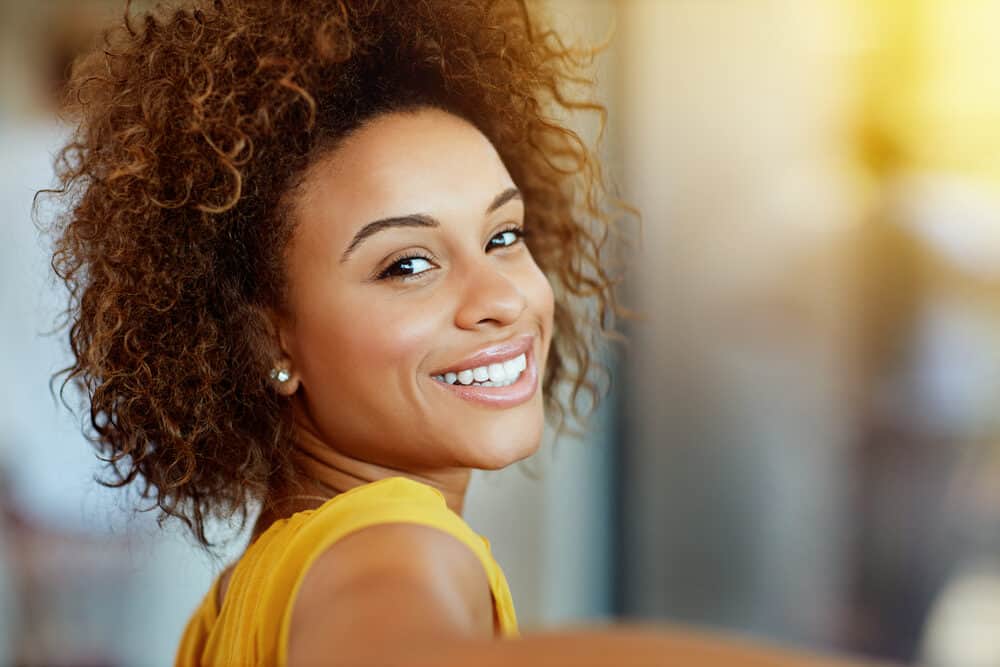 Attractive black woman wearing brown hair dye looking back over her right shoulder with a great smile.