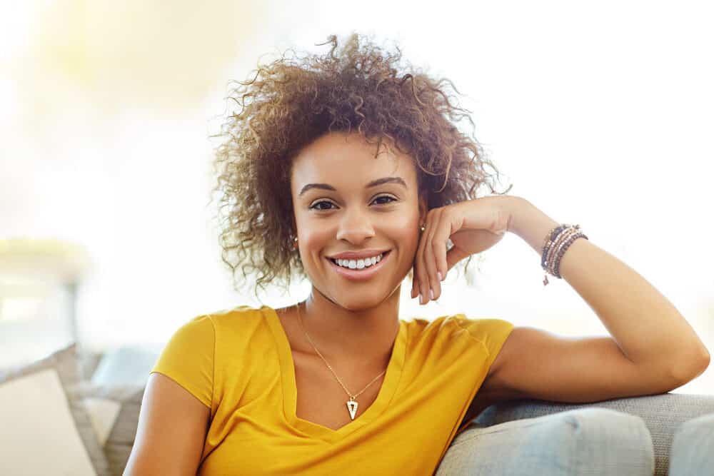 Light skinned black girl wearing multiple bracelets with blond hair on top of natural brown hair color.