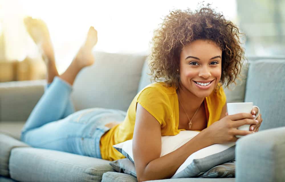 Young African American girl drinking a cup of coffee wearing a yellow t-shirt and blue jeans.