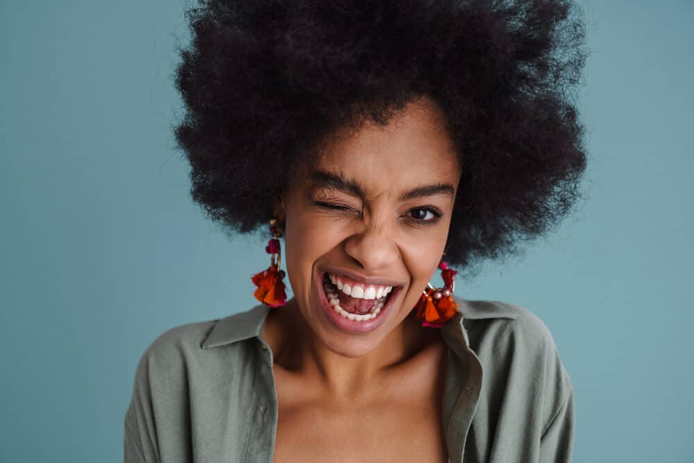 A playful black girl with big afro hair has her right eye closed as she makes a funny face.
