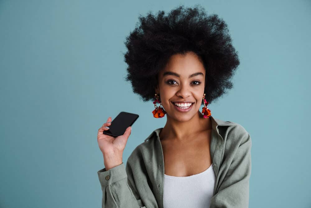 A lady with 4C African hair wearing an afro with red velvet earrings while making a phone call on her cell phone.