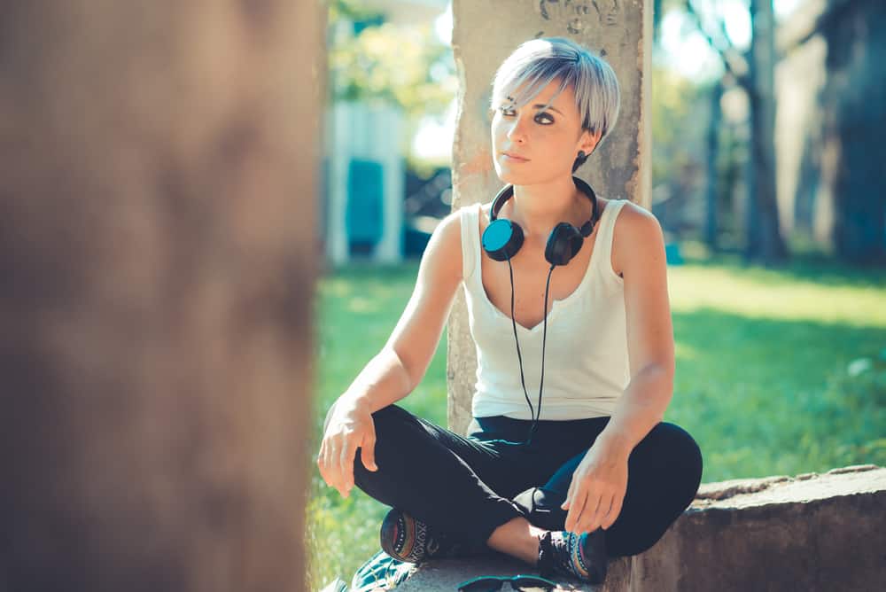 A lady with blue hair sitting with her legs crossed listening to her favorite music on headphones.