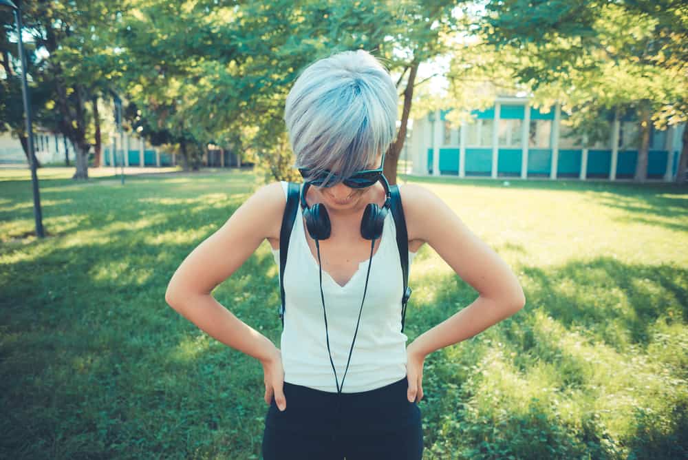 Cute woman with 1A hair type that's dyed her hair blue wearing headphones around her neck and a backpack.