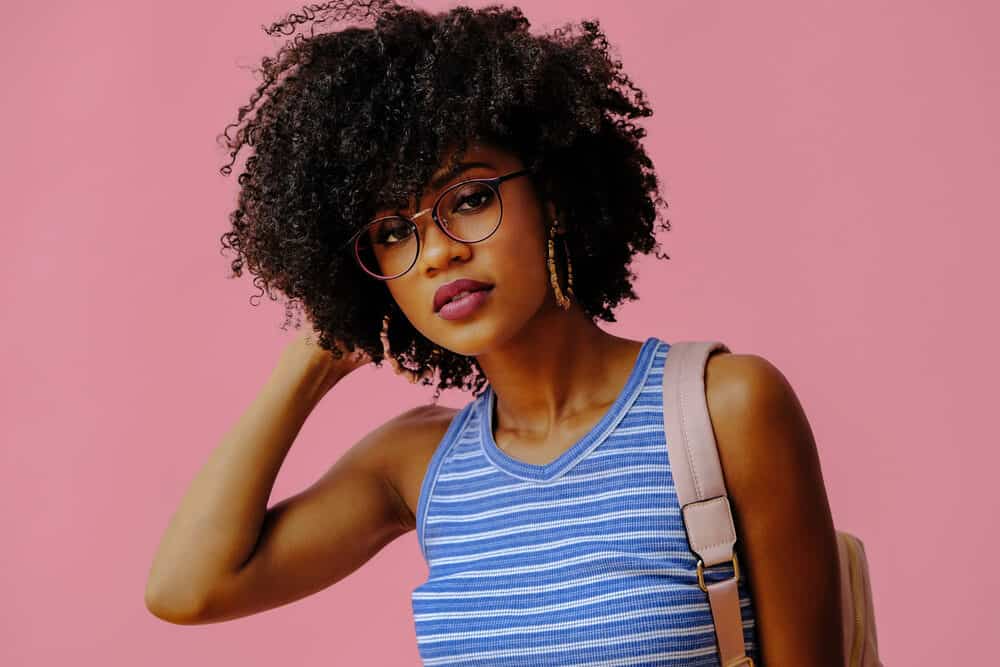 An African woman with medium-length hair growth wearing a blue and white shirt, red lipsticks, and gold earrings.