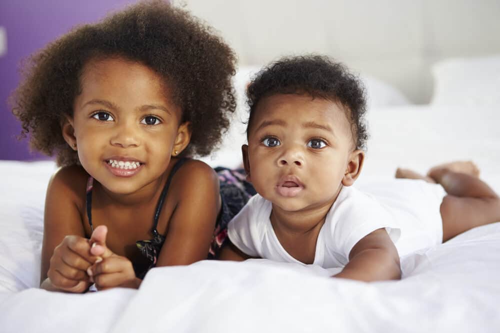 Two cute kids that are sisters posing for a photo as their mommy take the picture in the background.