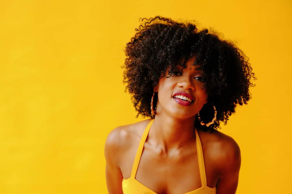 Cute African female with moisture-rich high porosity hair wearing a yellow casual shirt.
