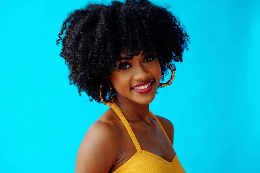 Cute African American female with a great smile wearing kinky 4A natural hair, gold earrings, and a casual shirt.