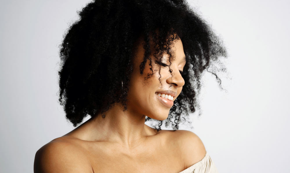 A cute African American lady wearing a casual beige shirt and natural lipstick has medium hair density.