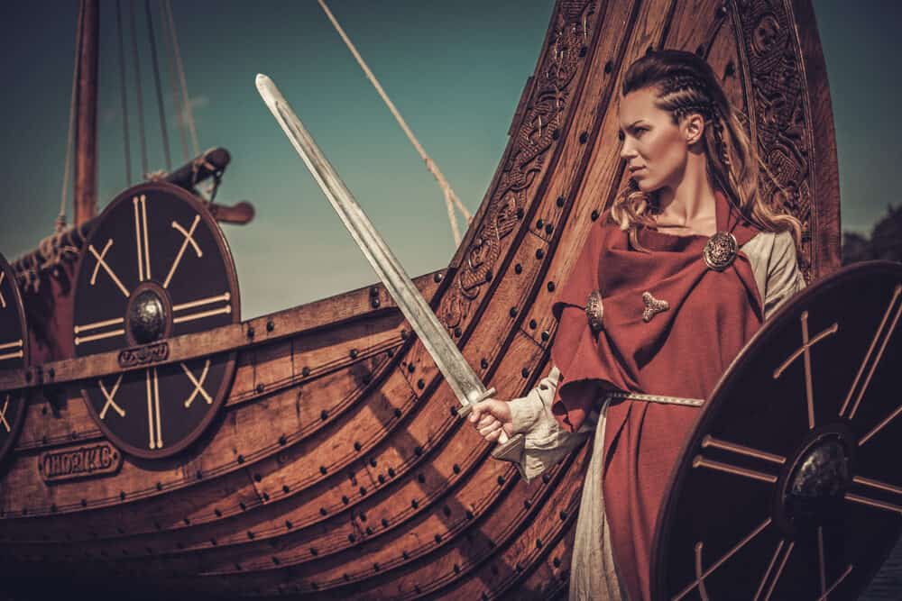 Confident Viking woman with braided hair holding off a series of enemies with her sword and shield.