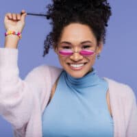 Cute black female with healthy hair showing her curly hair type and oily roots wearing pink eyeglasses.