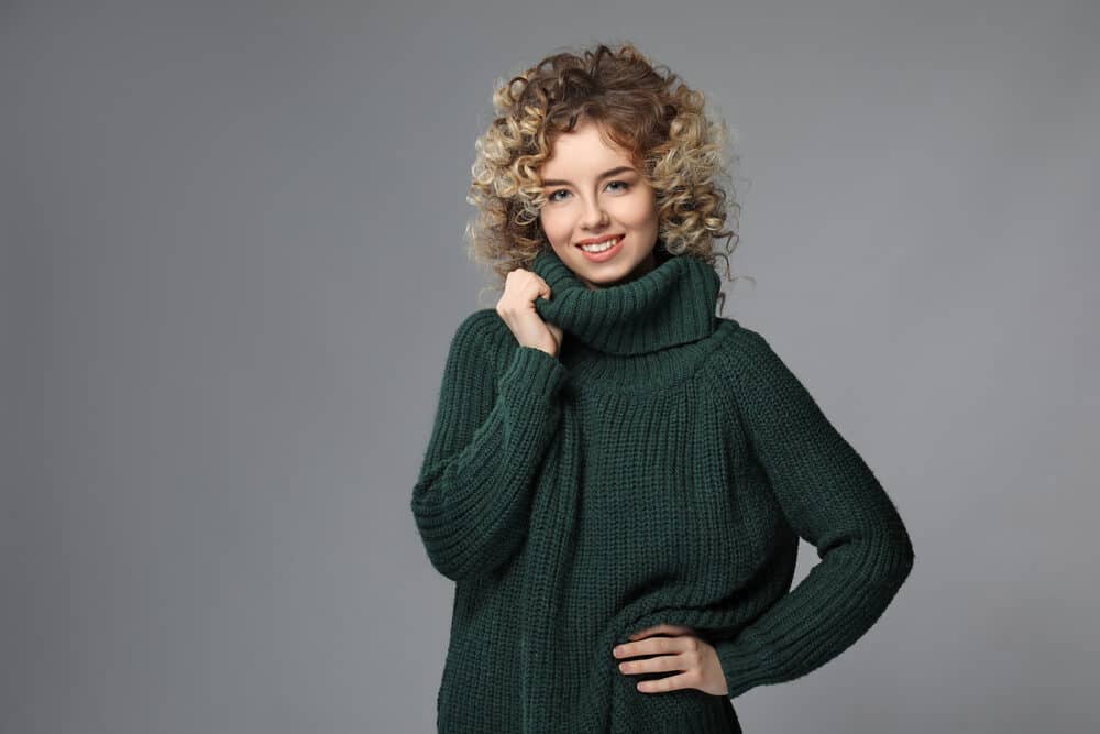 Young woman with tight curls 2C textured hair wearing a green casual sweater and lipstick.