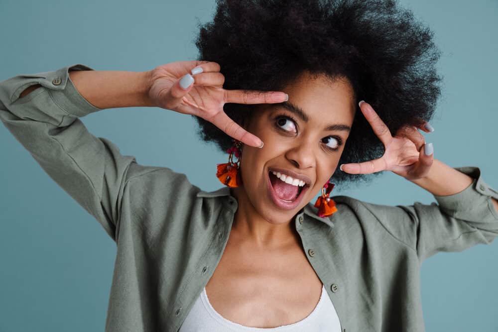 A black person with afro hair makes peace signs with her fingers.