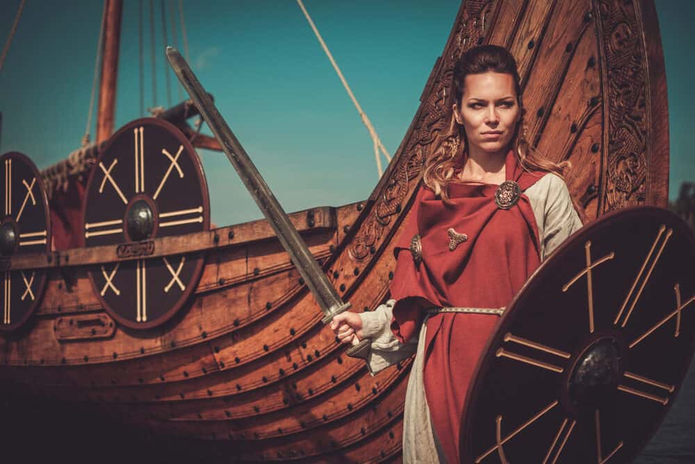 Viking woman with her hair braided wearing a red robe and beige war clothing.