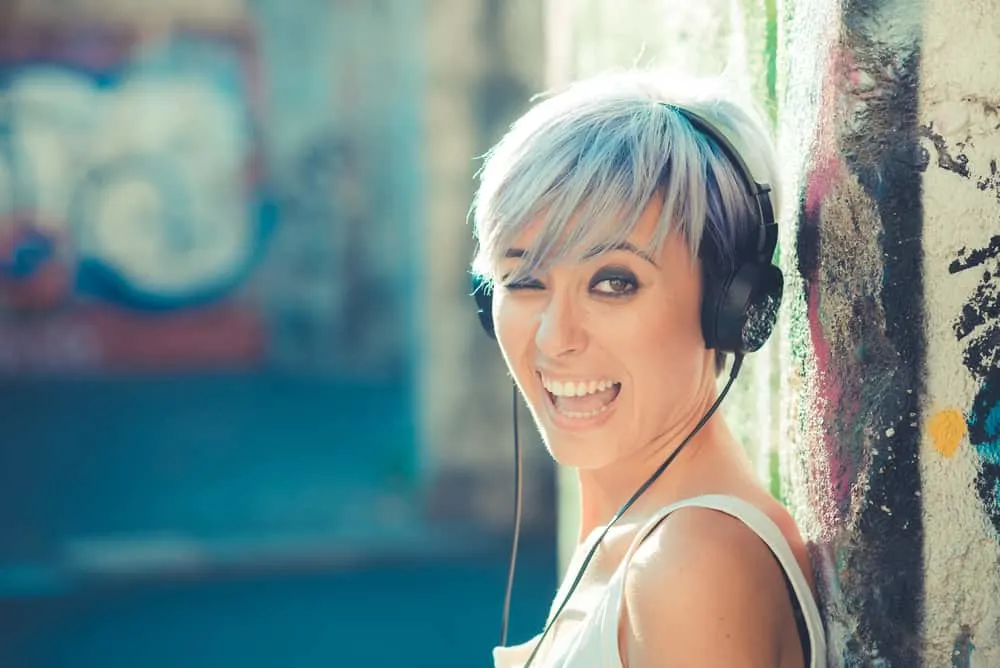 Hip young female with blue hair listening to rap music leaning up against a wall with graffiti.