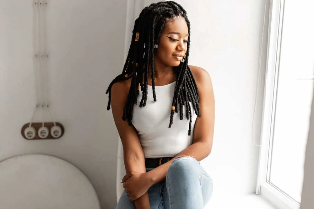 A gorgeous African American woman with rope-like locks of hair wearing a white t-shirt and blue jeans.