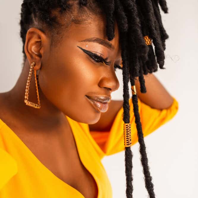 Happy African female wearing dreadlocks in an updo hairstyle adorned with gold jewelry.