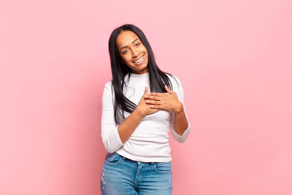 Young African American girl holding hands close to her heart that's concerned about hair follicle damage.