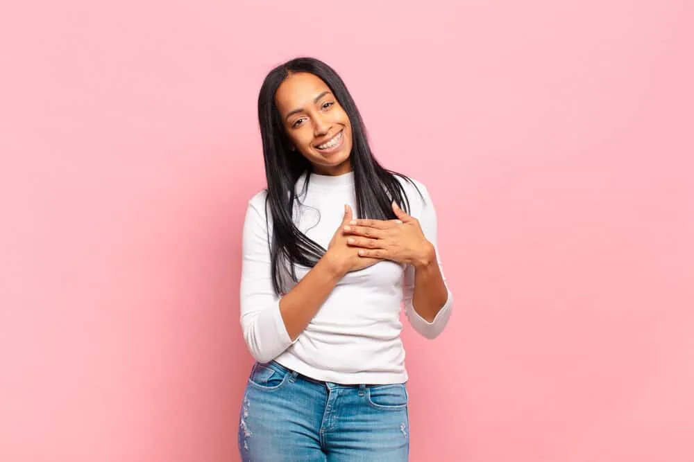 Can You Use Hairspray Before Straightening Your Hair? 7 Young African American girl holding hands close to her heart that's concerned about hair follicle damage.