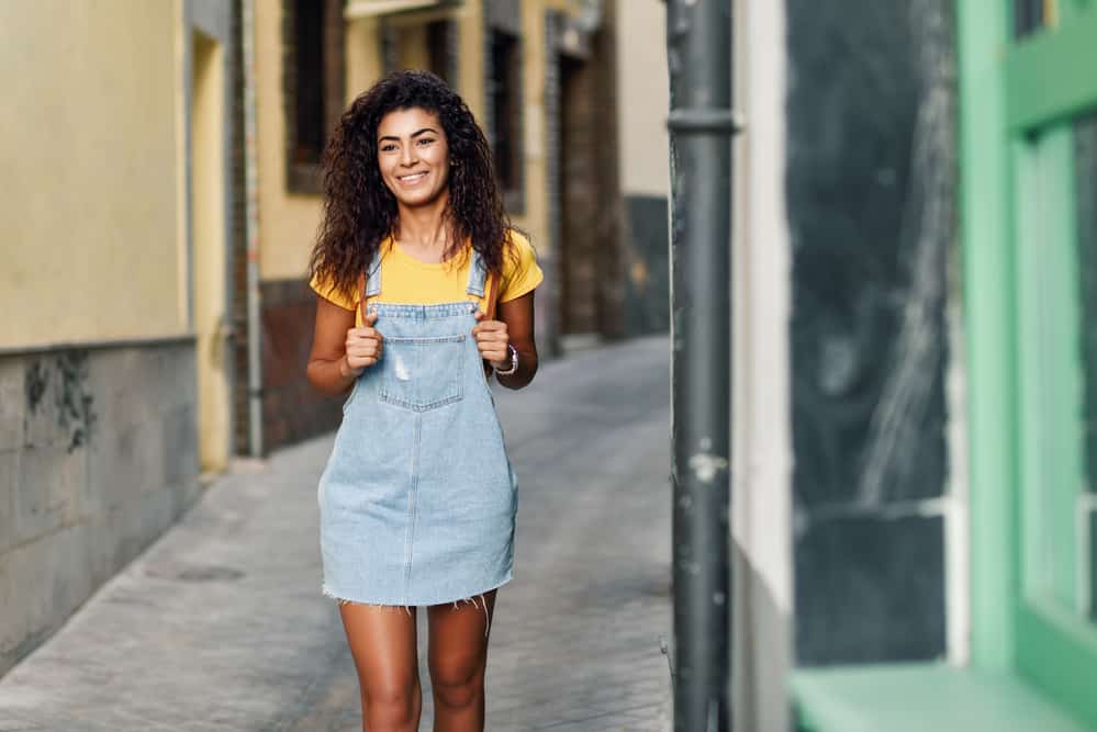 Young tourist with clean hair wearing a brown leather backpack and a torn overall skirt.