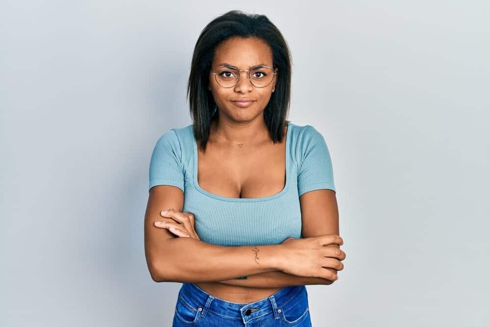 Black girl wearing her damaged hair natural with a blue shirt and round silver eyeglasses.