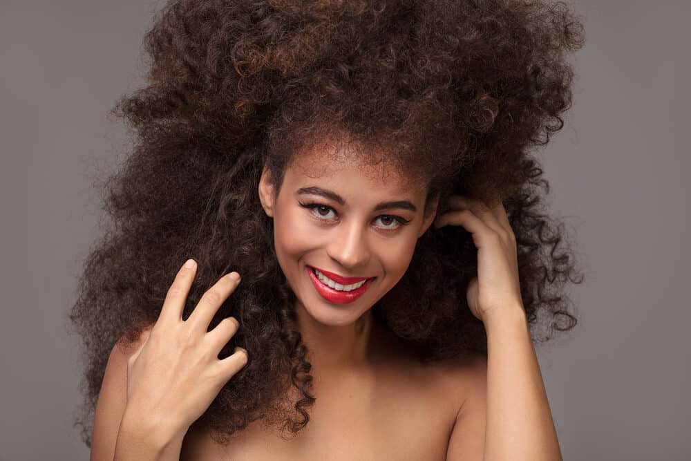 Cute African American female wearing a synthetic wig gently styled and combed with a wig brush.