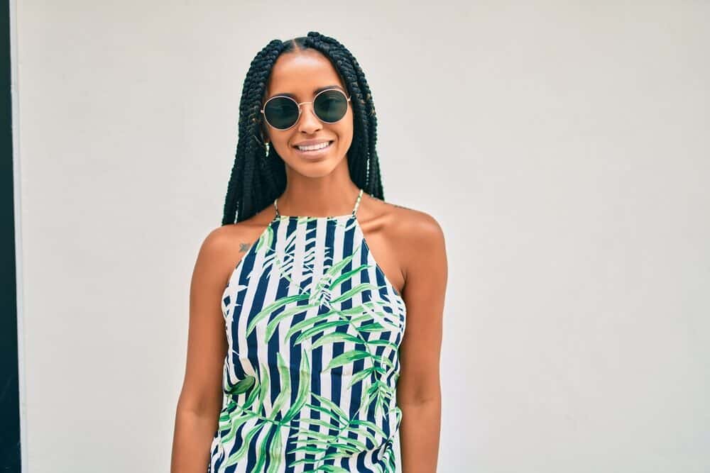 Young Hispanic woman wearing braids as a protective style and shades with gold rim.