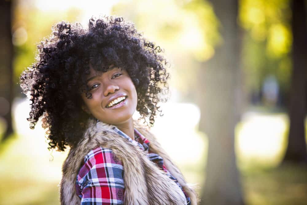 Female with curly natural hair wearing a plaid casual shirt and natural-looking make-up.