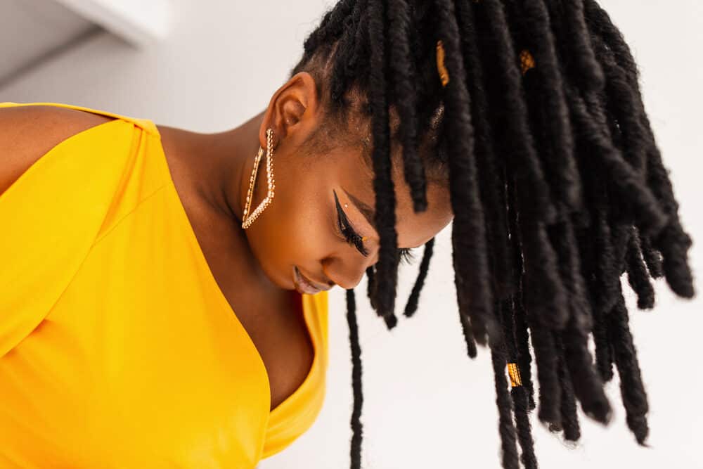 Beautiful woman with growing dreadlocks wearing gold earrings and a yellow dress.