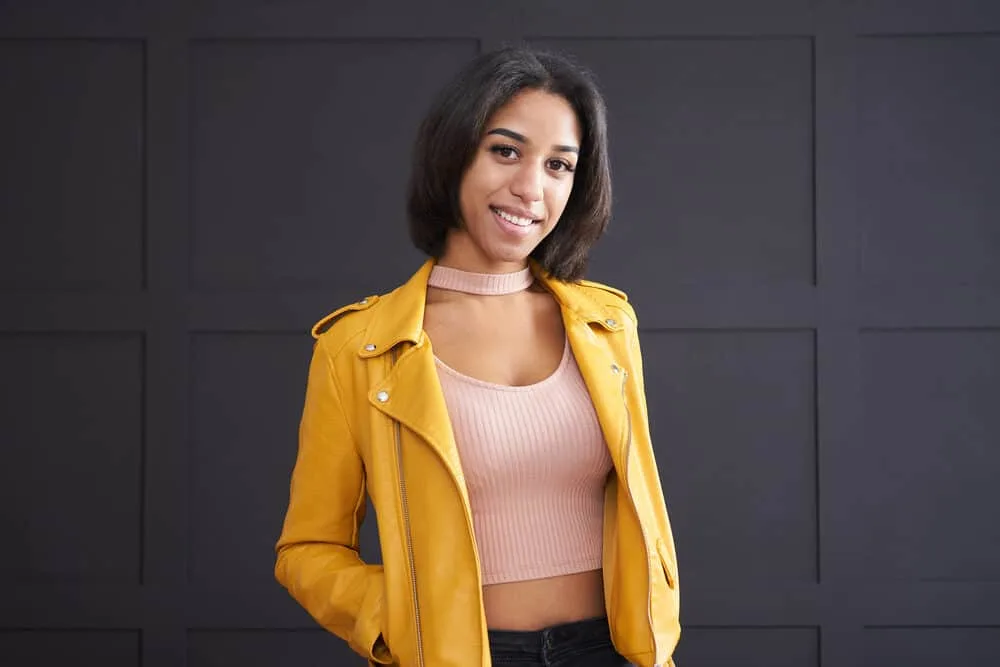 How Often Should You Flat Iron Your Hair (Without Damaging It) 3 A stylish young girl with thick hair and split ends wearing a yellow leather jacket and pink ribbed shirt.