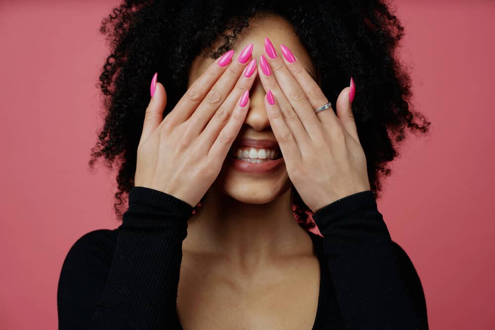 Adult woman with 4A curls wearing pink fingernail polish, red lipstick, and a black casual shirt.