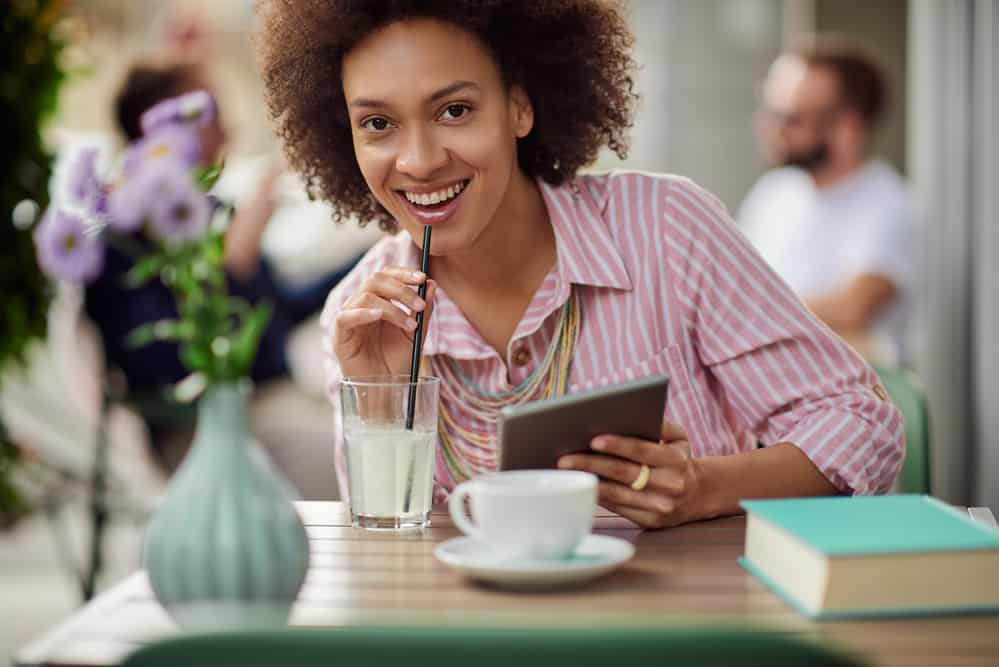 A cute mixed-race woman with a fair skin tone reading about how to dye her curls a blonde hair color on a tablet.