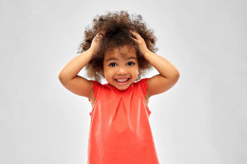A young black girl worried about potential hair fall holding her little bouncy girls up above her head.