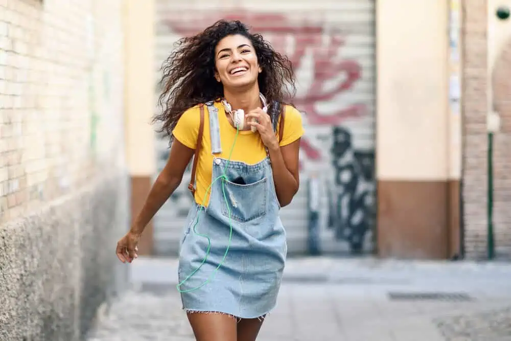How to Get Waves With Straight Hair for Beginners: Step by Step 1 Pretty young African American female with a wavy hair type wearing a blue jean dress and yellow t-shirt.
