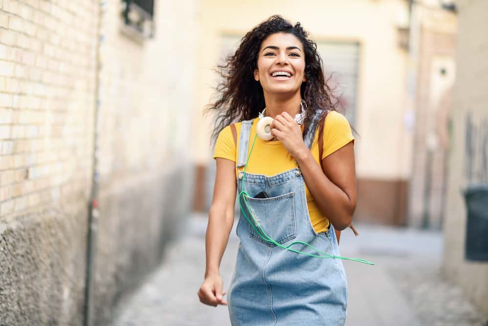 Cute black female with a natural wave curl pattern walking outside listening to music on her iPhone.