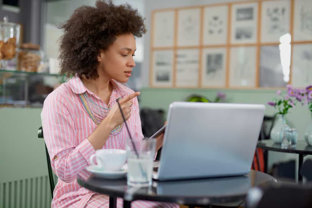 Woman wearing a dark brown hair dye color sitting in a coffee shop using a laptop researching cool skin undertones.