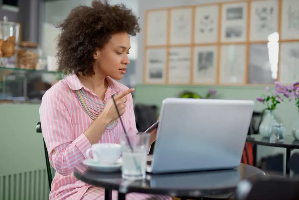 The 11 Best Unnatural Hair Colors for Cool Skin Tones 18 Woman wearing a dark brown hair dye color sitting in a coffee shop using a laptop researching cool skin undertones.
