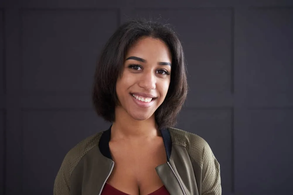 How Often Should You Flat Iron Your Hair (Without Damaging It) 4 African American woman wearing straight hair styled with coconut hair oil and stylish green jacket.