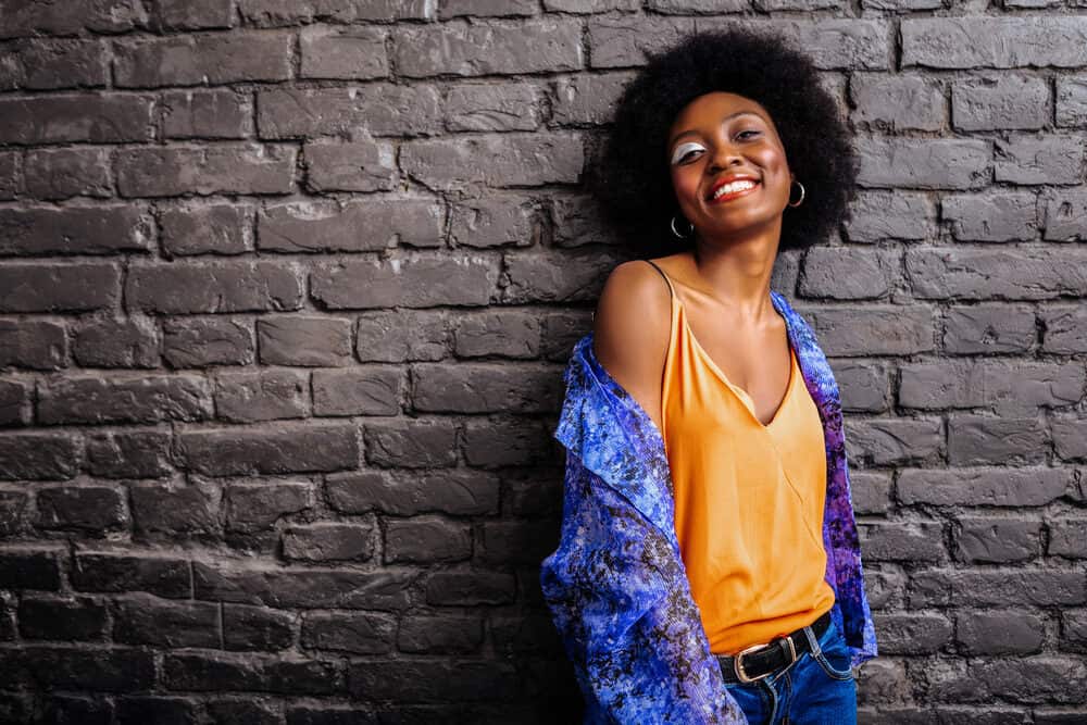 Adorable black lady with textured hair type wearing an orange shirt and blue jeans.