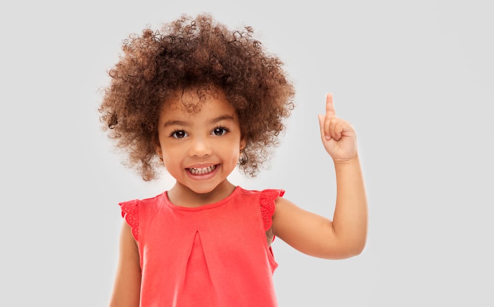 Little baby girl with super curly hair pointing her finger up.