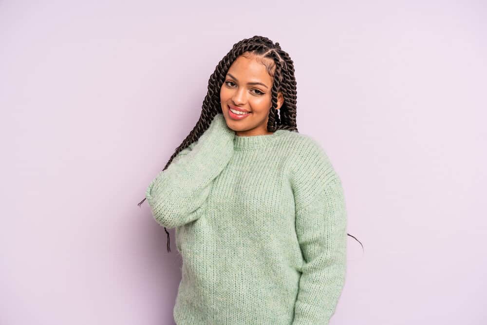 Mexican female mixed with African descent with thick hair in medium braids wearing a green sweater.