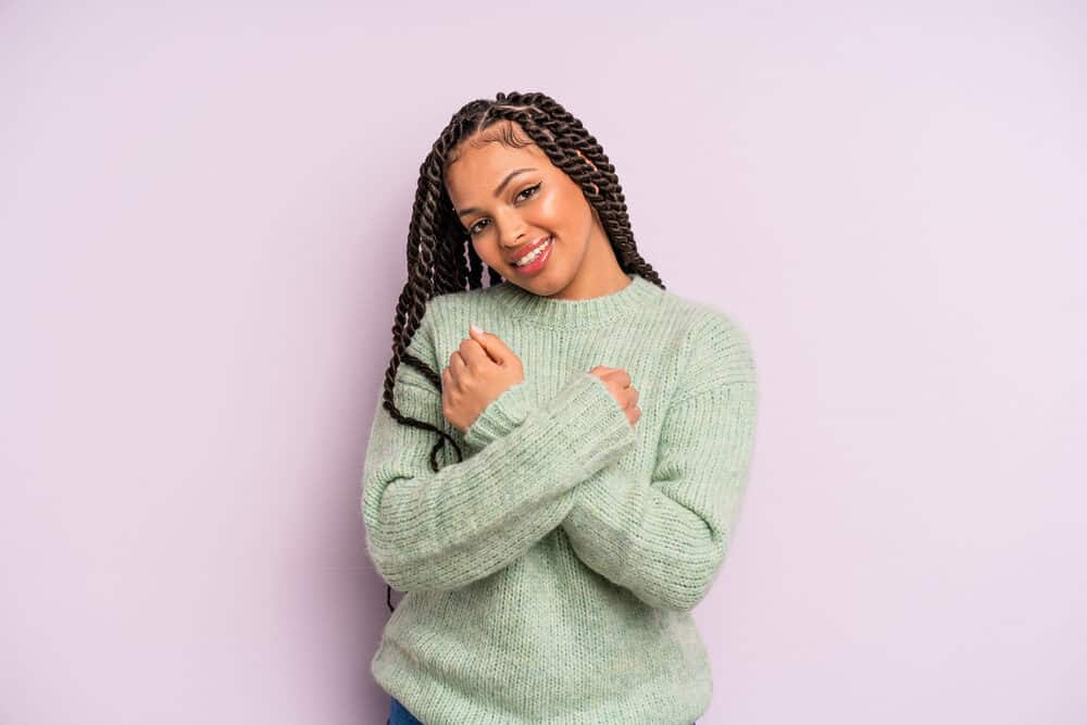 Young light-skinned Latina female wearing a stylish look with Mexican braids and a green knitted sweater.