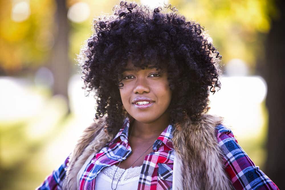 A black lady with curly hair loss is seen wearing a kinky hair wig and casual clothes.