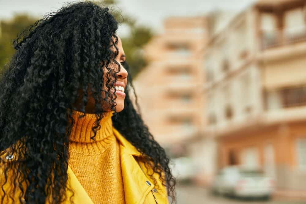 African American woman wearing a yellow sweater and jacket with a curly wig secured with a wig clip.