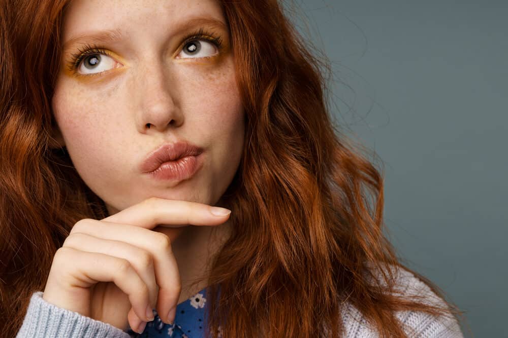 A young puzzled woman with bright orange 1C hair strands wearing a subtle pink lipstick.