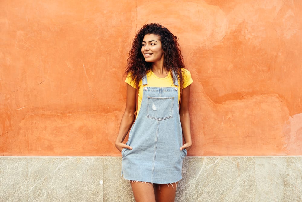 A lady with perfect waves on a medium curl length wearing a casual blue jean outfit.