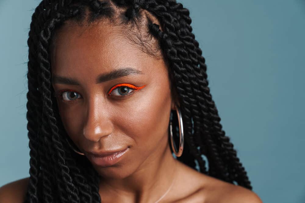 Black woman with box braids and a stressed scalp wearing red eye shadow and silver hoop earrings.